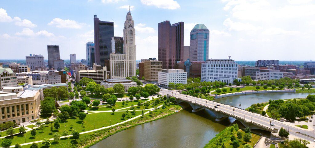 Downtown Columbus skyline with modern buildings, green parks, and the Scioto River, representing a vibrant urban atmosphere near attractions and walkable neighborhoods.