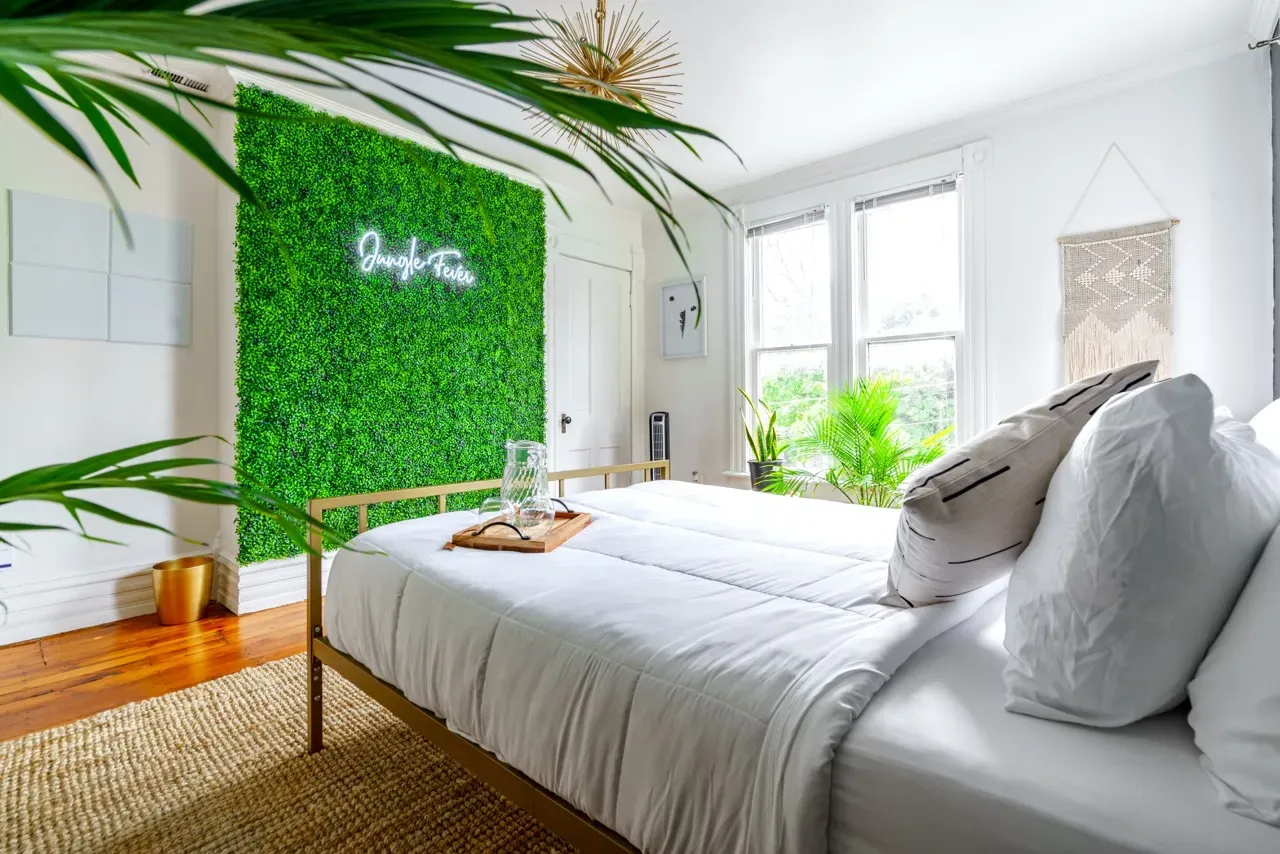 Cozy bedroom at Jungle House featuring a green moss wall, modern decor, and natural light from large windows, highlighting luxury vacation rental ambiance in Columbus, Ohio.