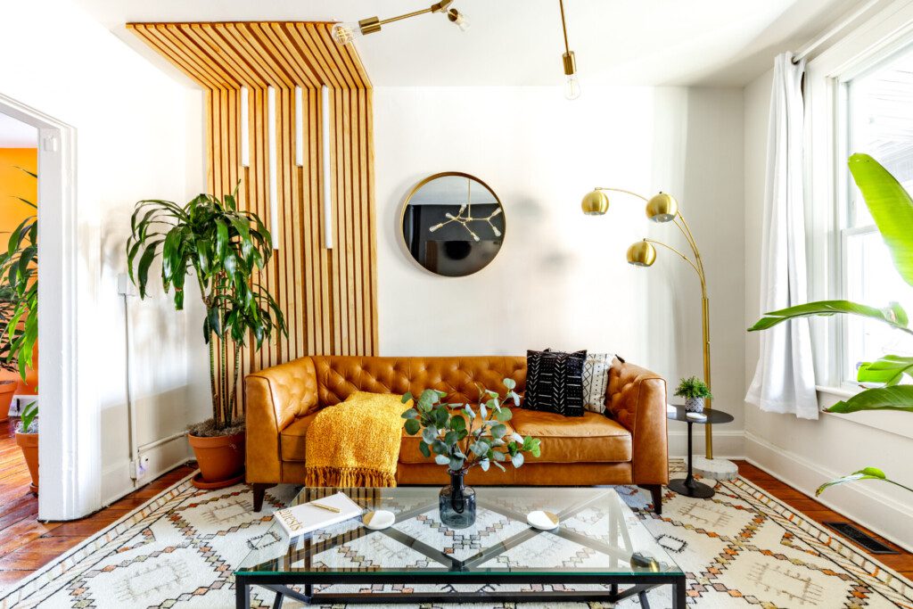 Stylish living space in Jungle House featuring a brown leather sofa, decorative pillows, a glass coffee table, indoor plants, and modern lighting, emphasizing comfort and aesthetic appeal for boutique vacation rentals in Columbus.